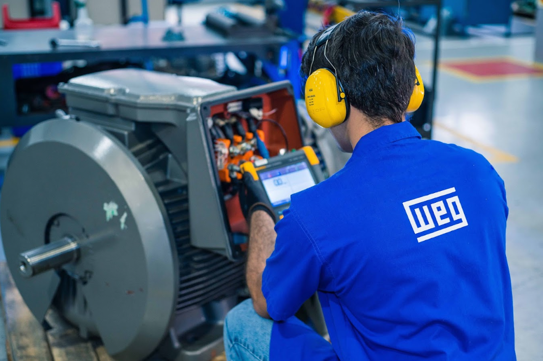 Technician performing electric motor repair with diagnostic test equipment in an industrial facility.