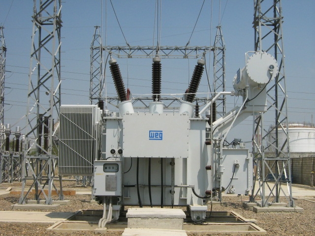 Outdoor industrial power transformer installed at a substation, surrounded by high-voltage lines and support structures.