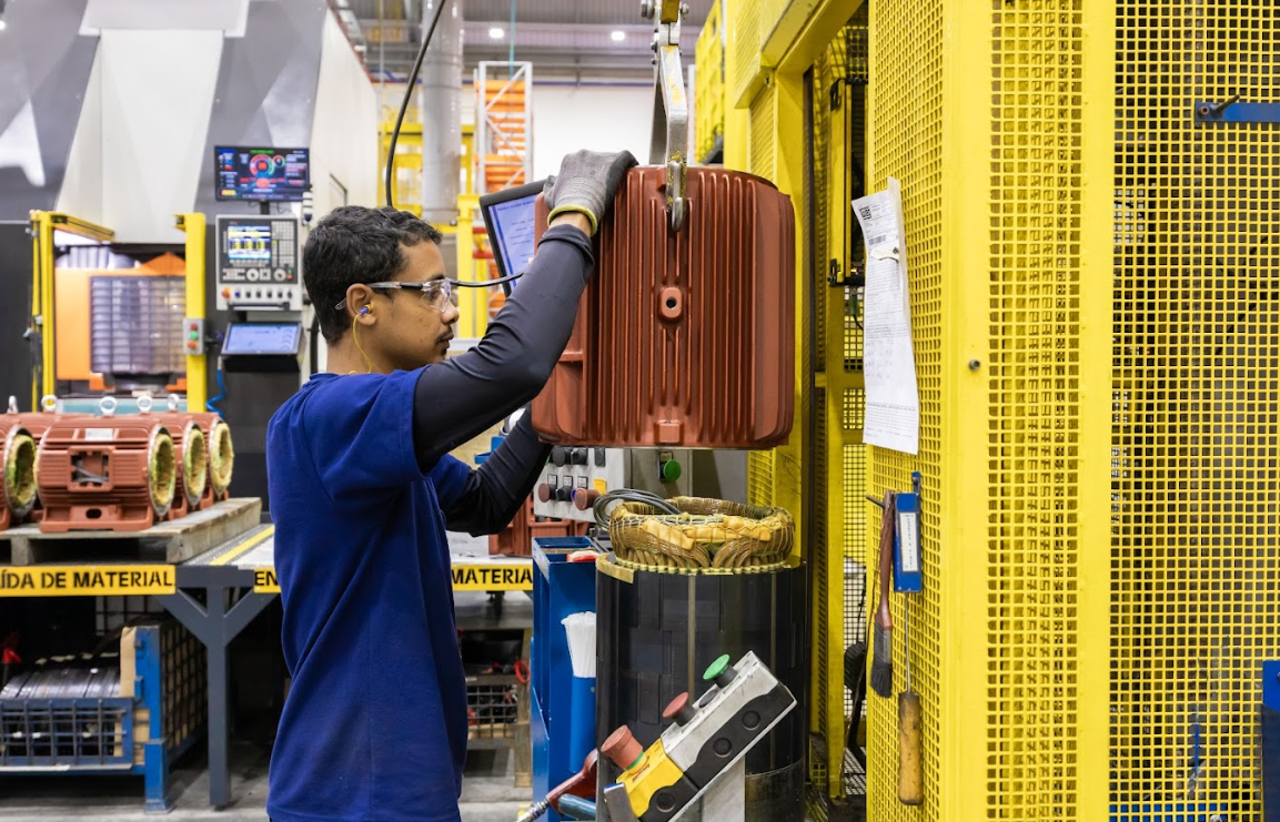 Technician working on a high-efficiency electric motor in a factory environment with monitoring equipment.