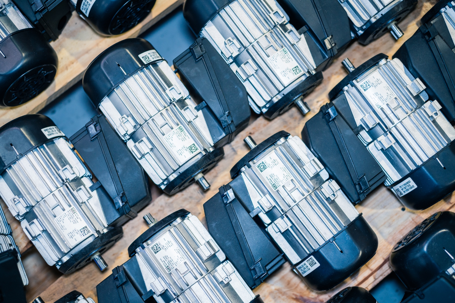 Cluster of electric motors organized in uniform rows, arranged on a wooden pallet for industrial assembly.