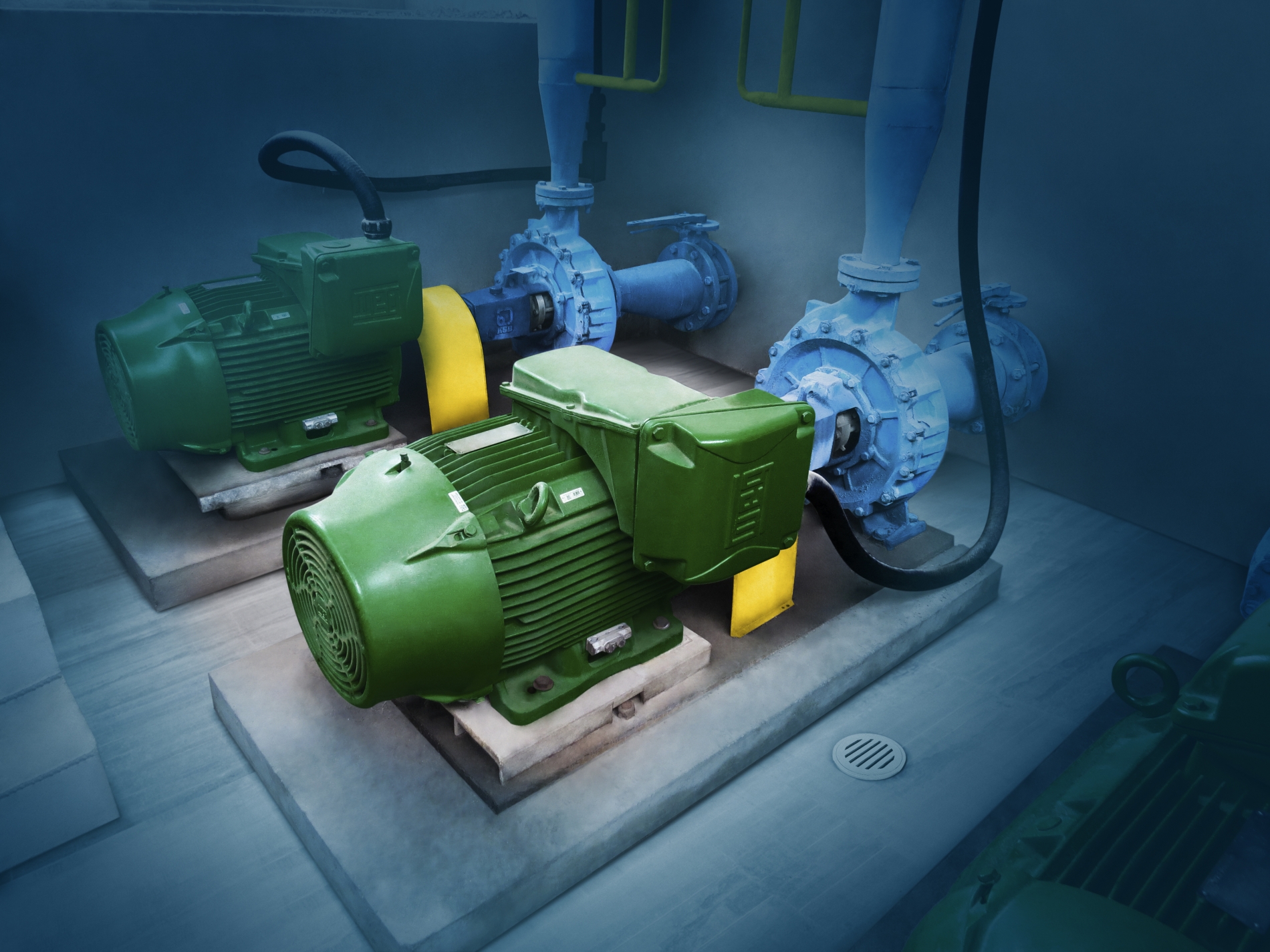 Multiple green industrial electric motors installed in a moisture-prone, enclosed pump system environment.