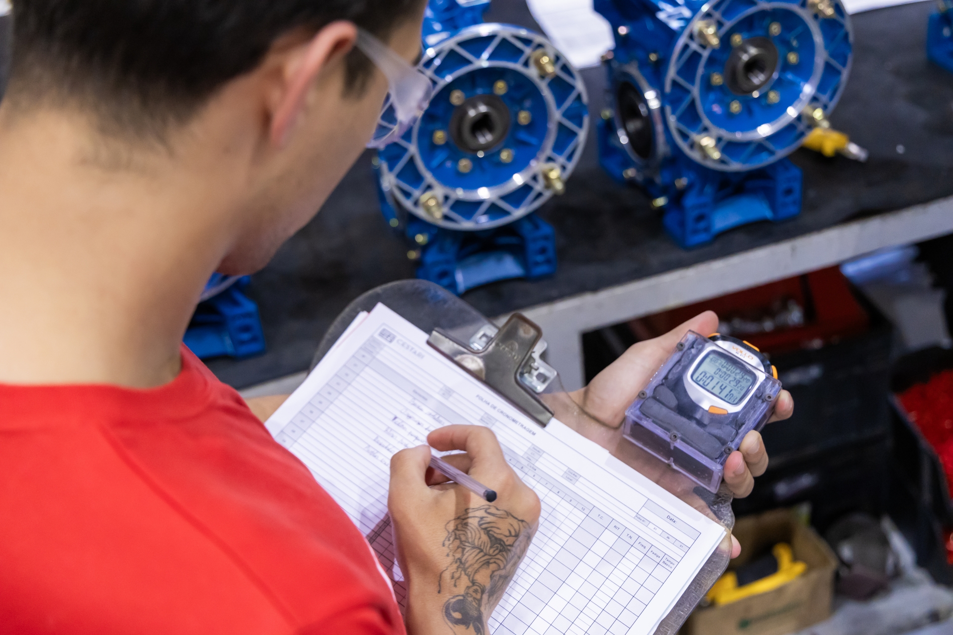 An engineer reviews the performance data and specifications of electric motors, using a stopwatch and checklist to perform the task.