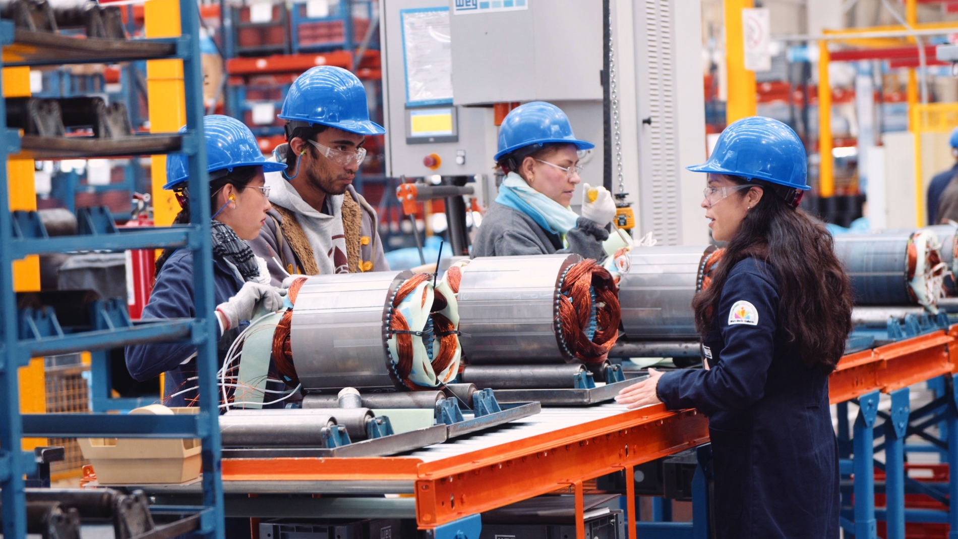 An engineering team lead discusses the assembly of electric motors with her team, showcasing motors with visible copper windings and shaft components.