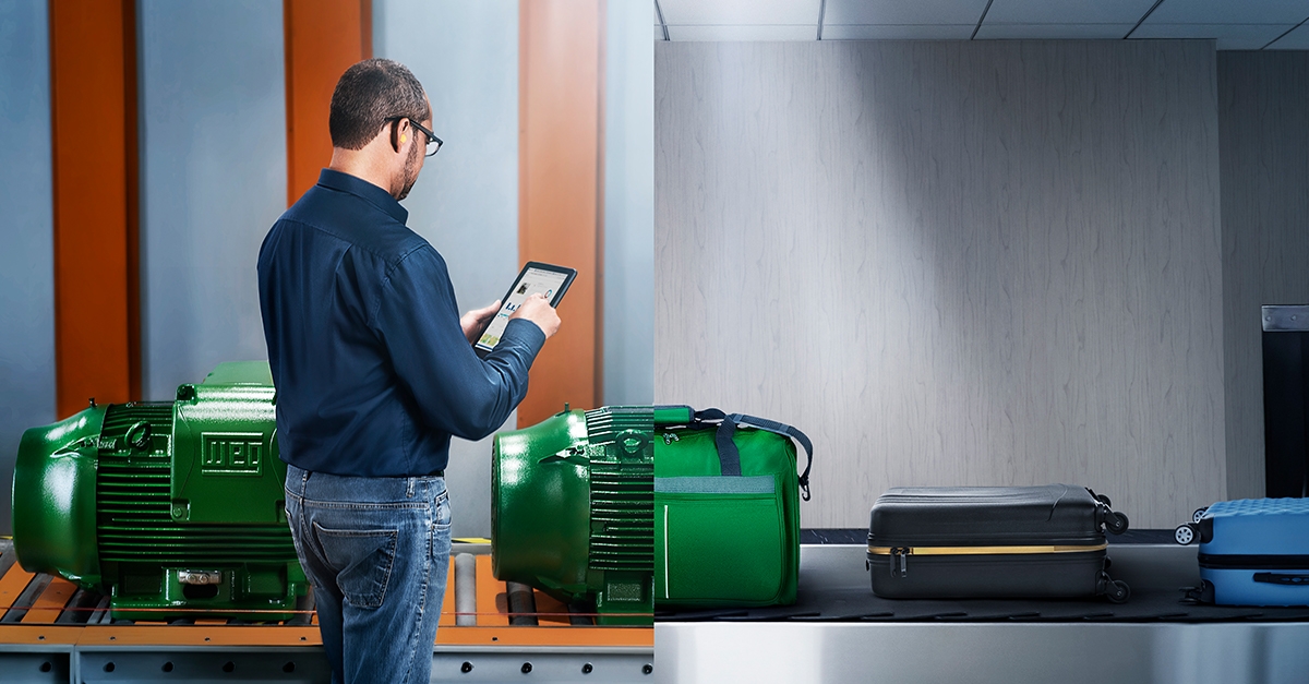 Technician using a tablet to monitor performance of industrial green electric motors beside a conveyor system.