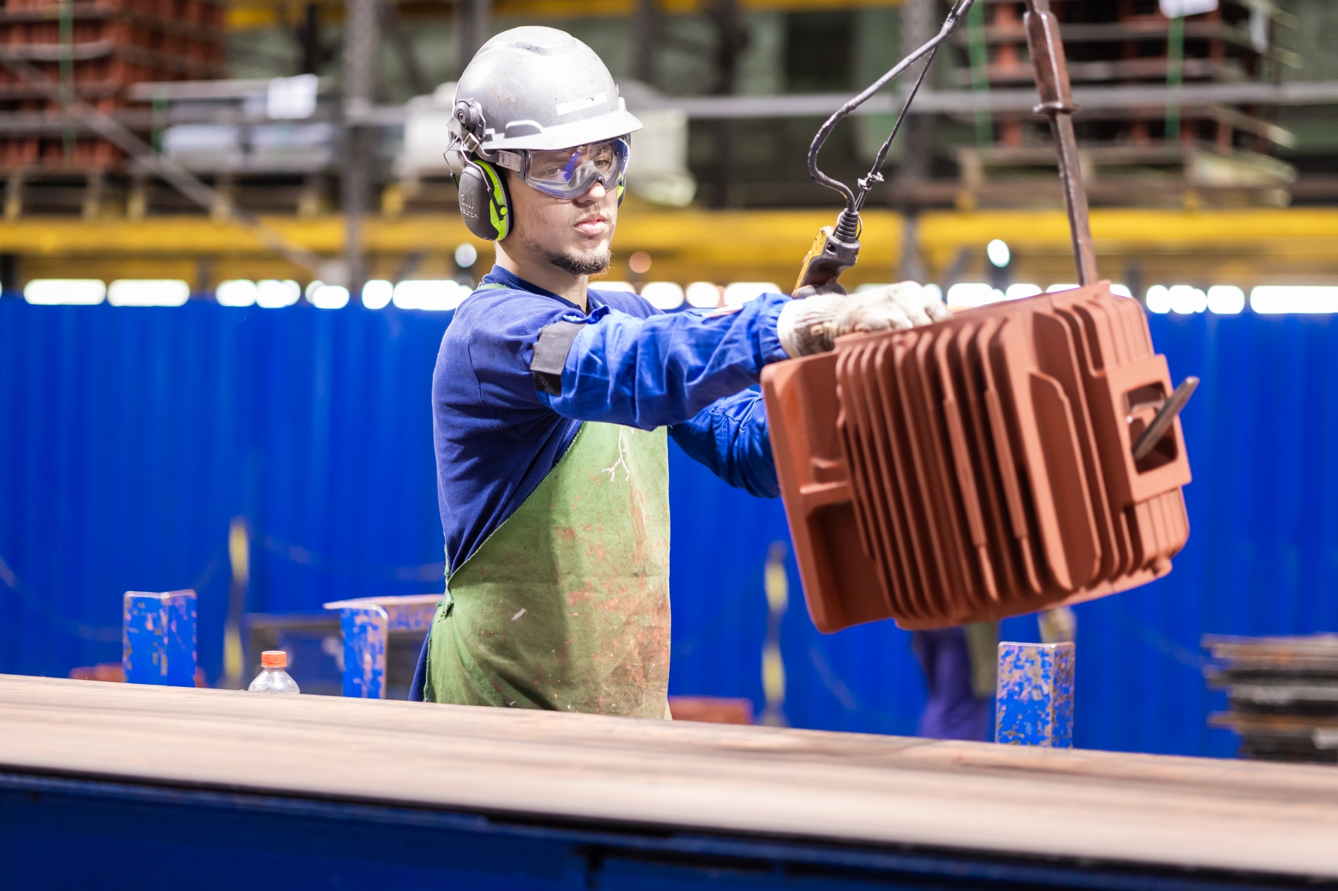 Engineer in protective gear performing maintenance on an industrial electric motor housing in a factory environment.