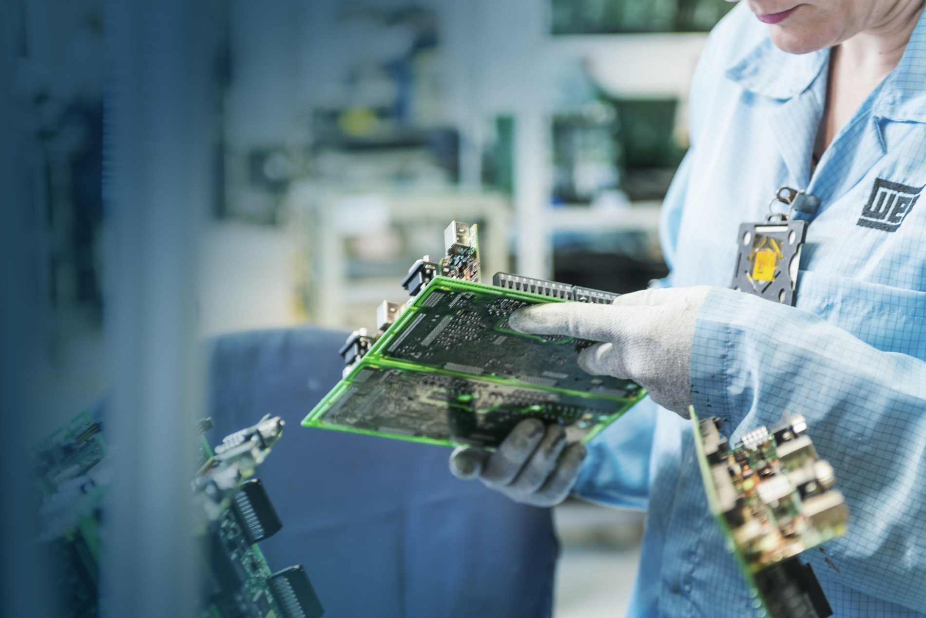 Technician in a laboratory environment inspecting a green circuit board, emphasizing precision and quality control in electric component manufacturing.