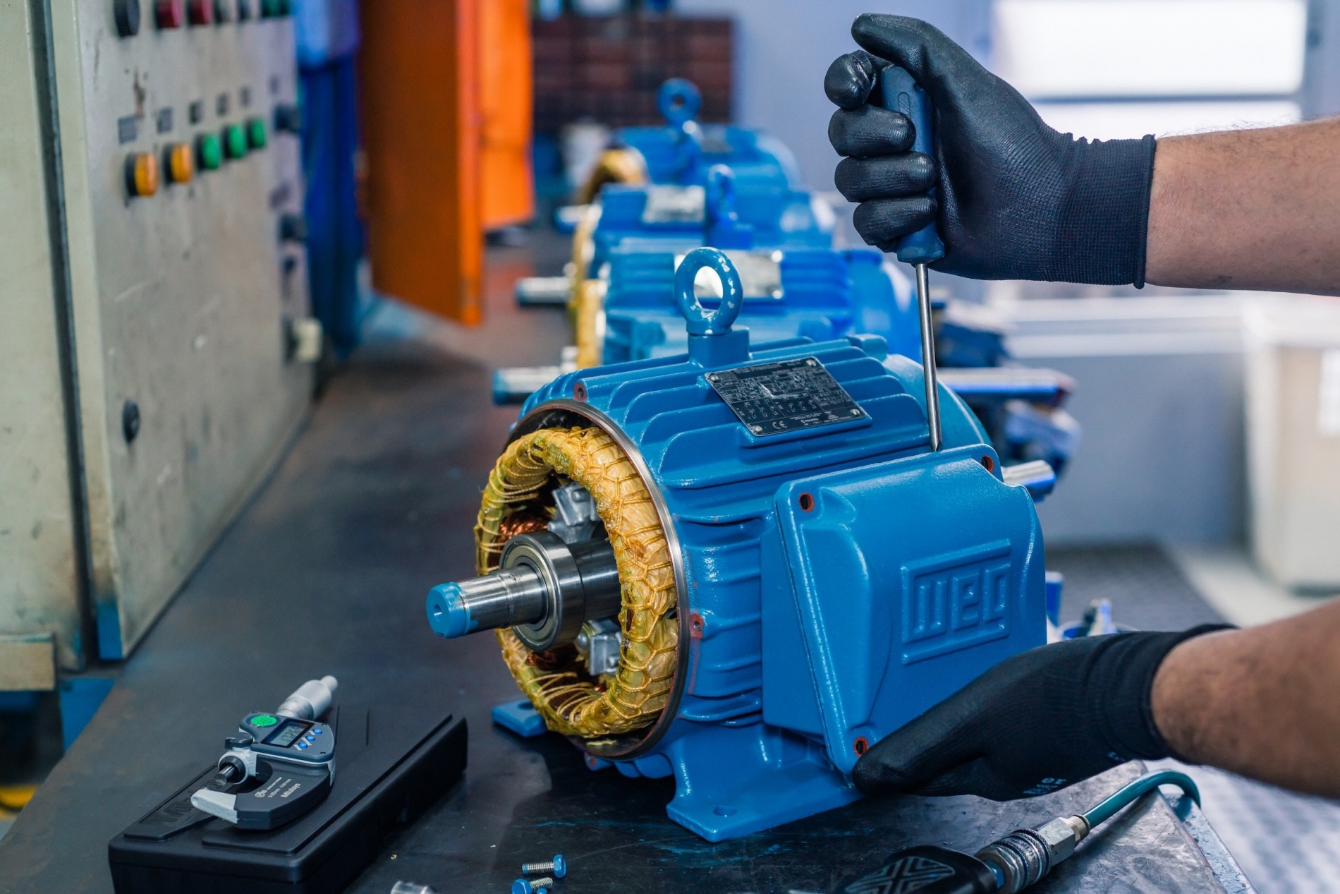 Close-up of a blue WEG electric motors component being serviced with hand tools in a workshop.