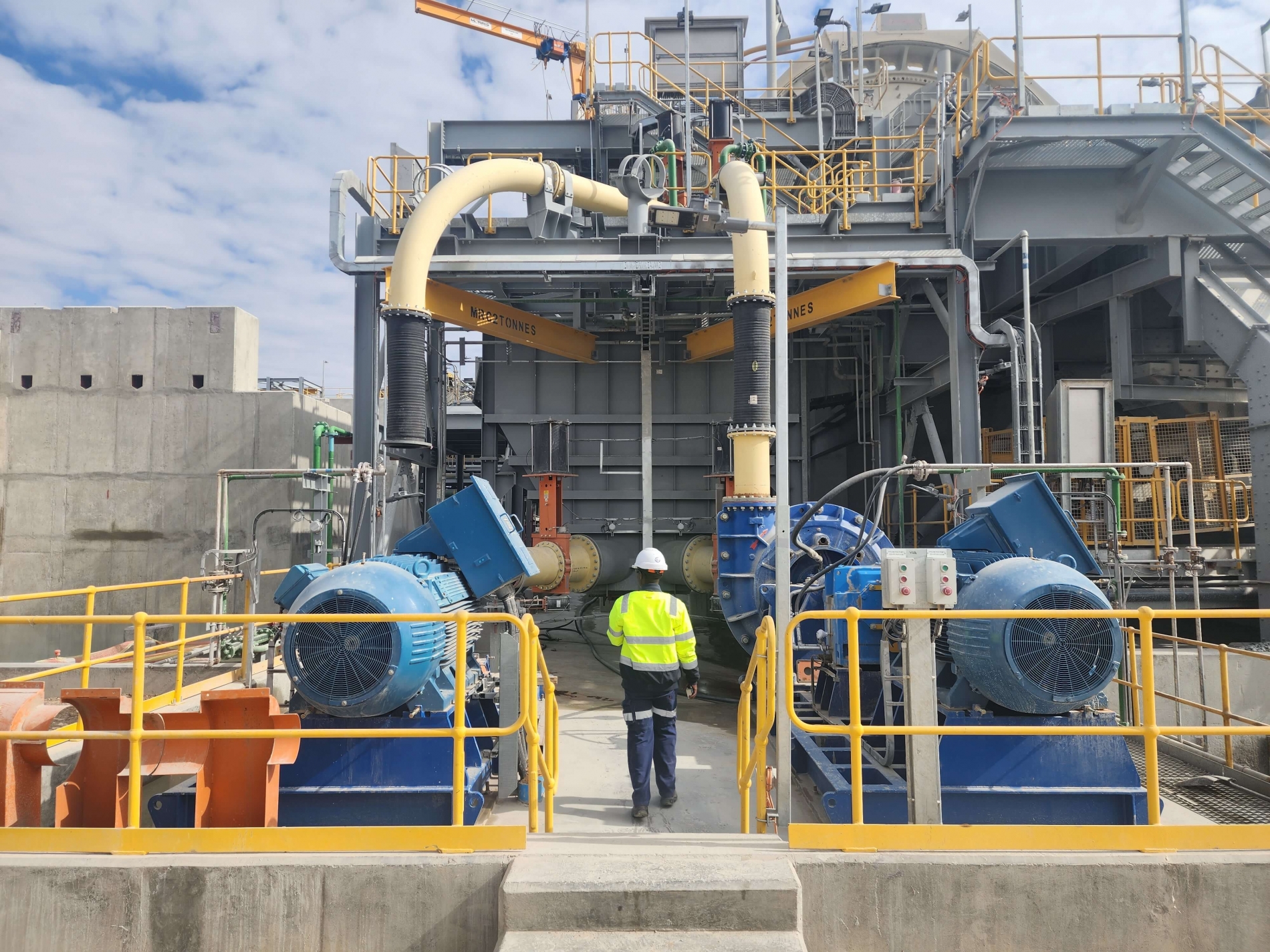 Worker walking past large industrial electric motors and piping at an outdoor automation facility.