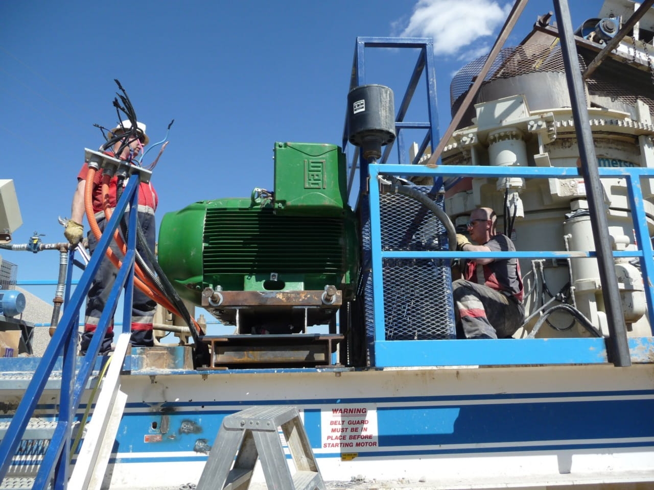 Technician inspecting an industrial electric motor on-site, checking enclosure risks to industrial motor performance.