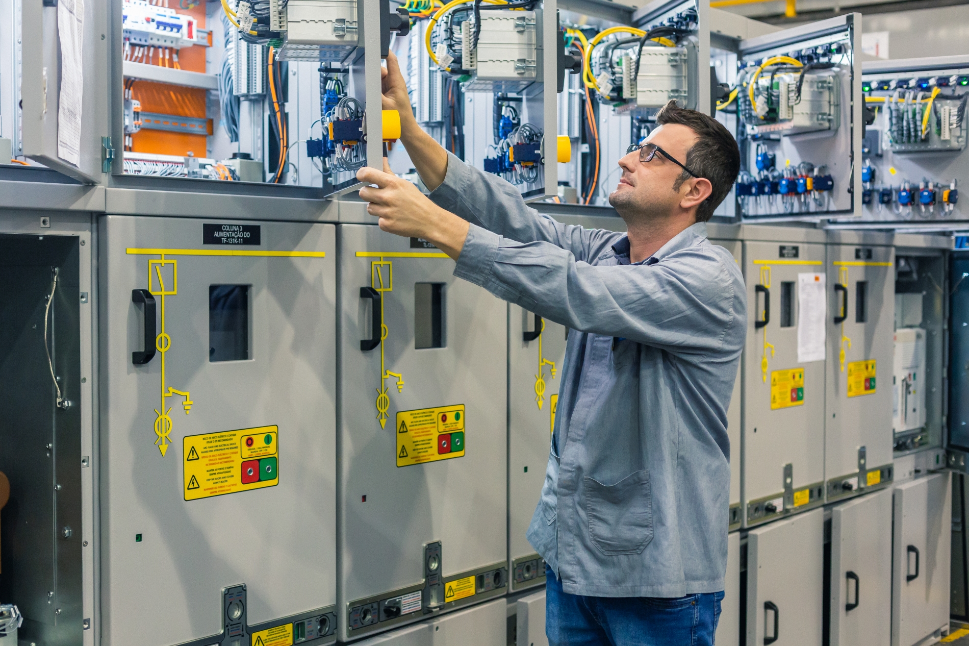 An engineer inspects an open VFD control panel in an industrial setting with electrical motors and high-voltage equipment.