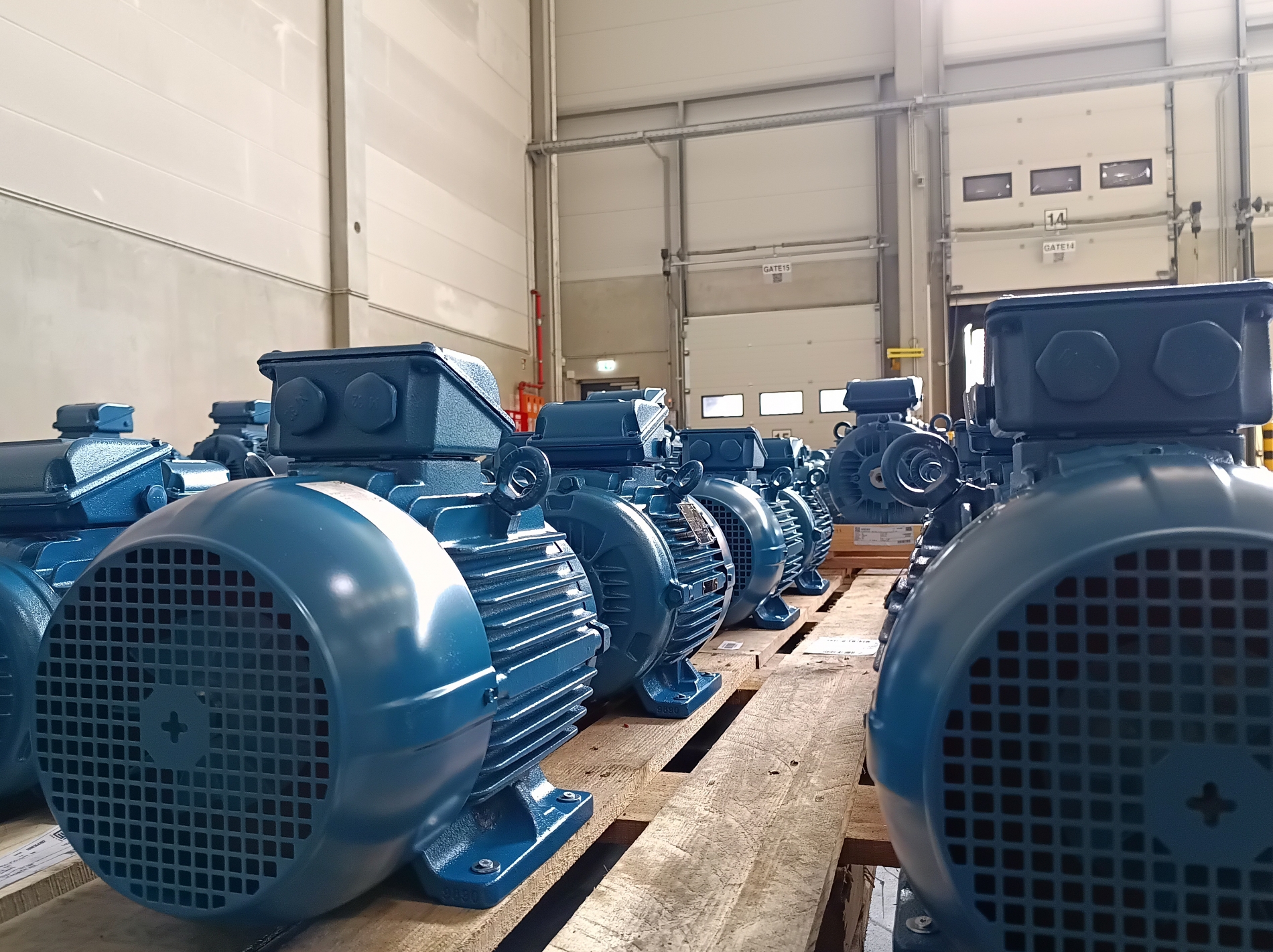 Row of high-efficiency industrial electric motors installed on wooden pallets inside a factory.
