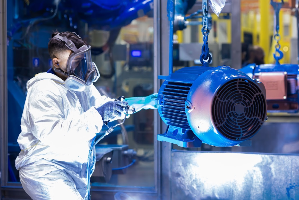 Technician in protective gear working on a TEFC electric motor inside an industrial facility, showcasing detailed motor components and safety procedures.