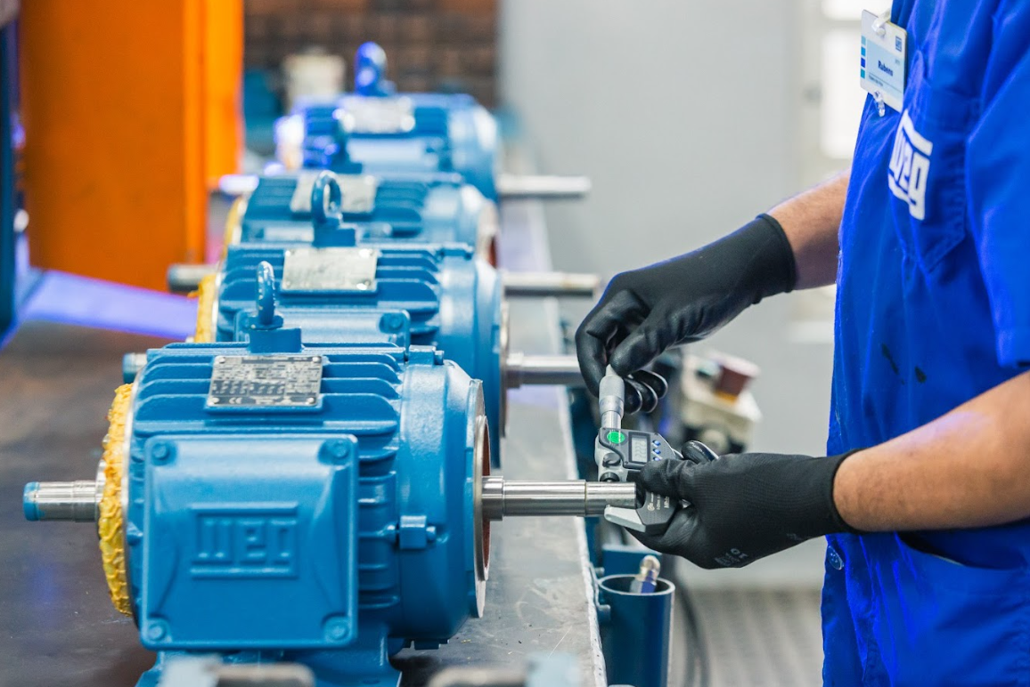 Technician using precision tools to inspect the shaft of a WEG W22 electric motor during the quality control process in a manufacturing facility.